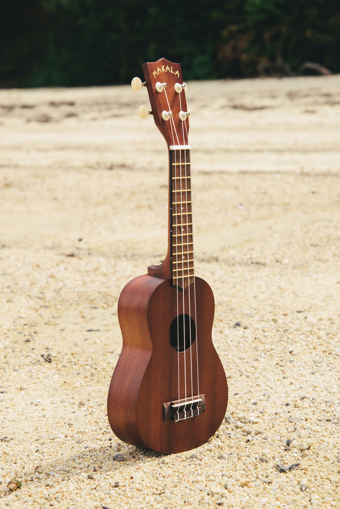 A Makala Soprano Ukulele shown on a beach at a right angle.