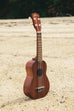 A Makala Soprano Ukulele shown on a beach at a right angle.